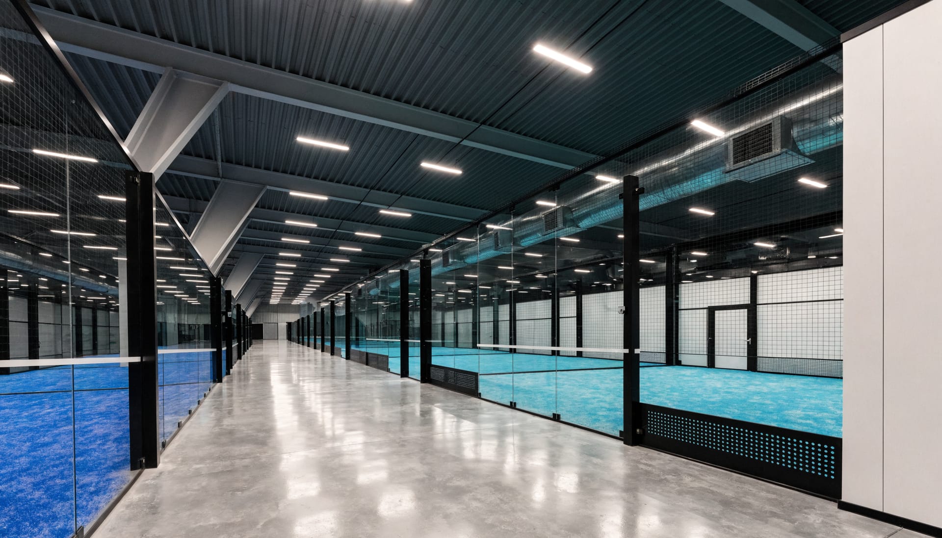 Leere, hell beleuchtete Padelhalle mit mehreren Plätzen hinter Glaswänden
